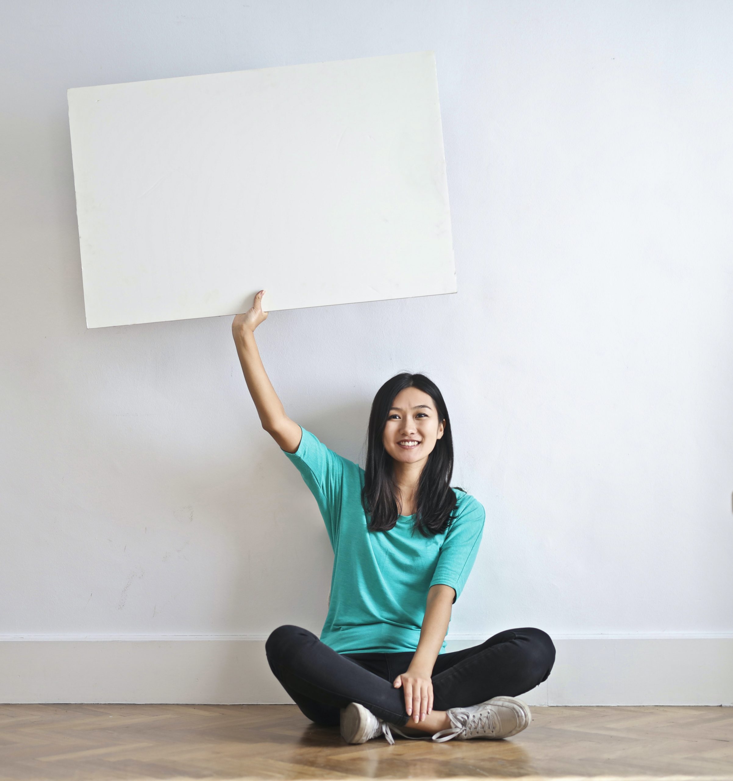 Woman sitting on the floor and holding up an empty sign