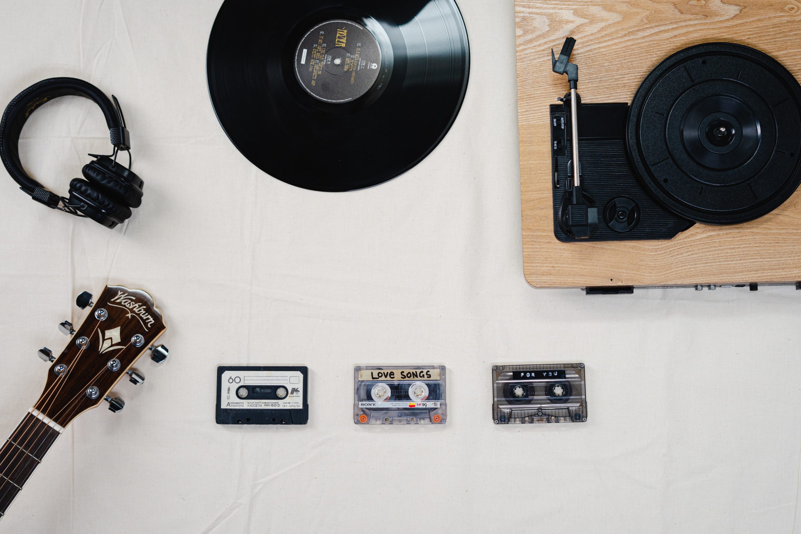 A record, cassette tapes, record player, and headphones laid out on a table