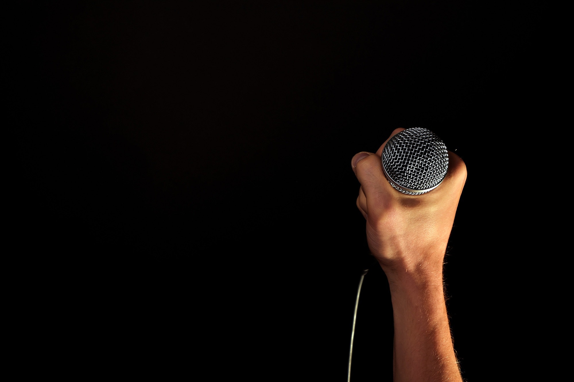 A hand holding a microphone in front a black background