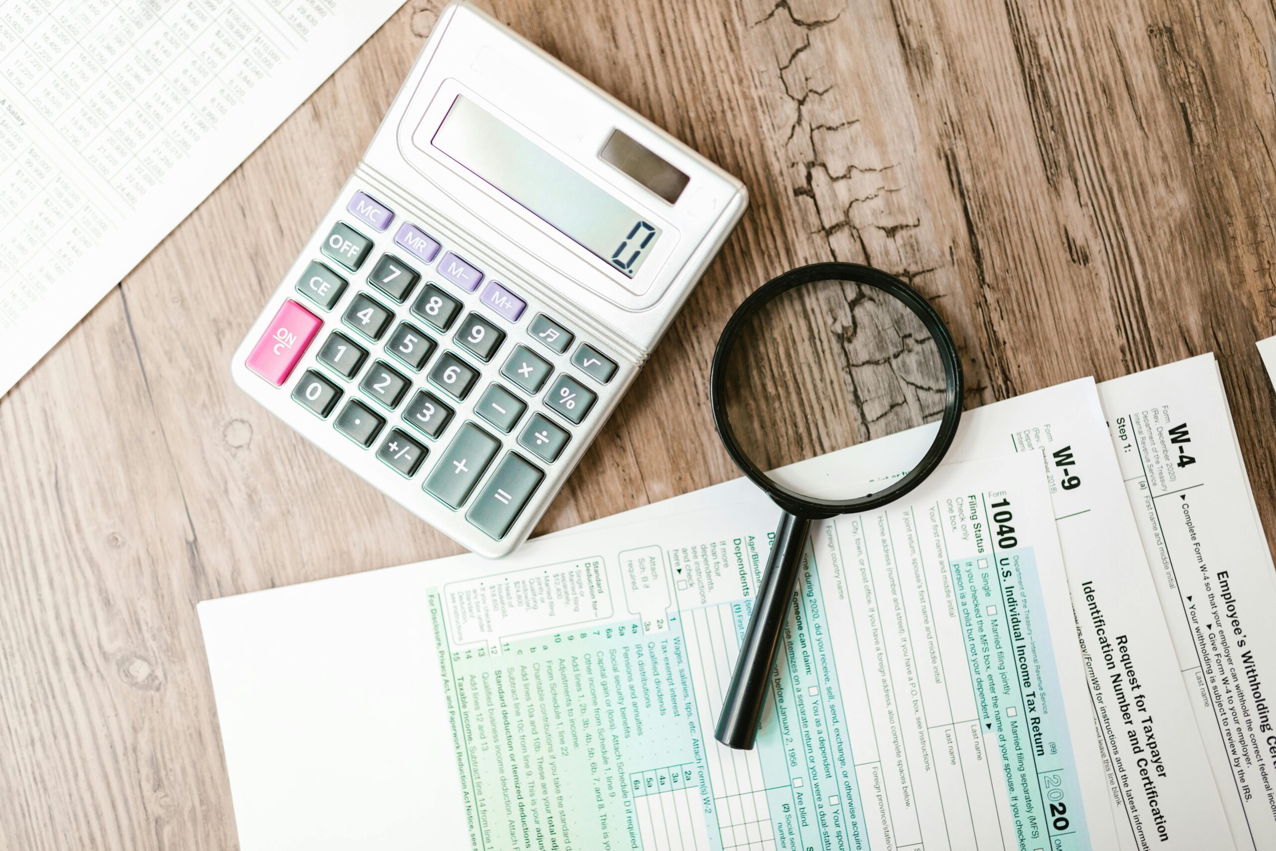 Calculator, magnifying glass, and paper on a table.